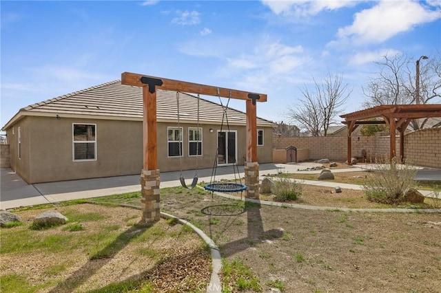 rear view of property with a trampoline, fence, stucco siding, a pergola, and a patio