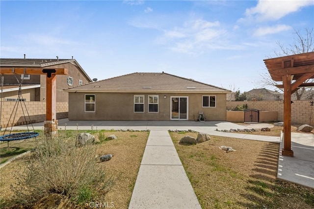 rear view of house featuring a patio area, stucco siding, a fenced backyard, and a trampoline