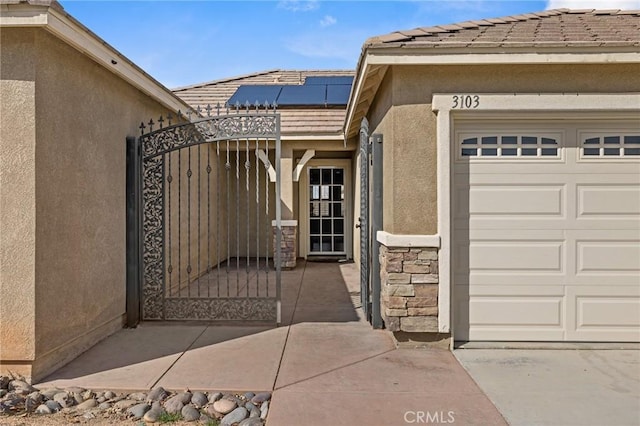 view of exterior entry with a gate, stucco siding, stone siding, a tiled roof, and roof mounted solar panels