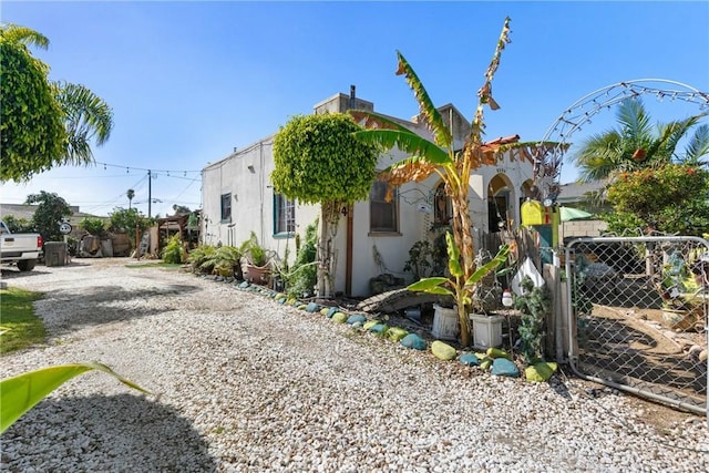 view of side of property featuring stucco siding, fence, gravel driveway, and a gate