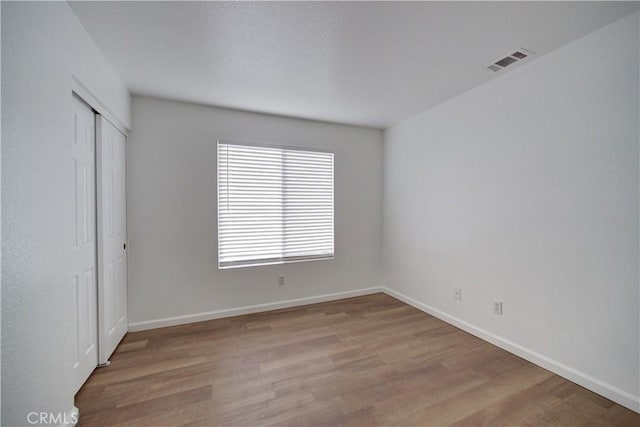 unfurnished bedroom featuring a closet, visible vents, baseboards, and wood finished floors