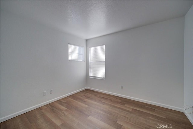 unfurnished room with a textured ceiling, baseboards, and wood finished floors