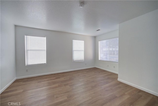 unfurnished room with visible vents, a textured ceiling, baseboards, and wood finished floors