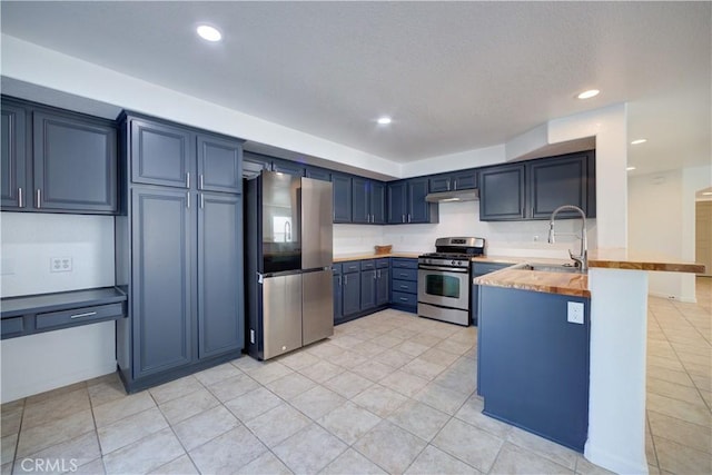 kitchen featuring under cabinet range hood, appliances with stainless steel finishes, a peninsula, blue cabinets, and a sink