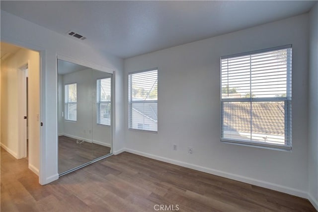 unfurnished bedroom with wood finished floors, visible vents, a closet, and baseboards