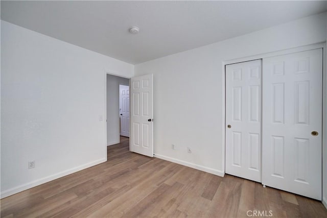 unfurnished bedroom featuring wood finished floors, baseboards, and a closet