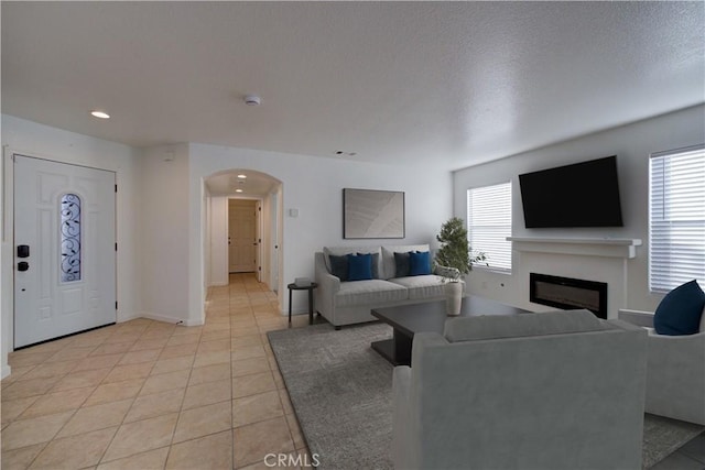 living area with a glass covered fireplace, light tile patterned floors, a healthy amount of sunlight, and arched walkways