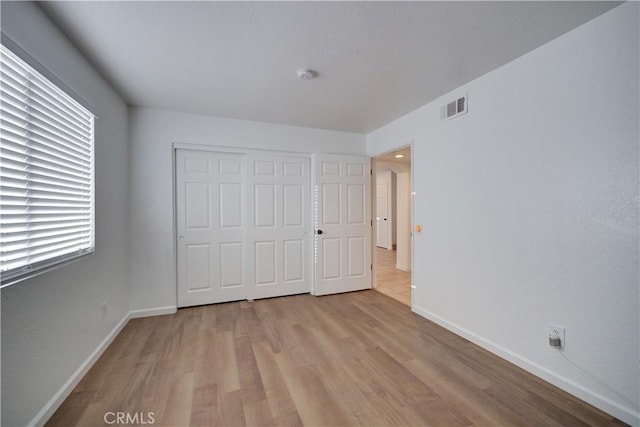 unfurnished bedroom with visible vents, baseboards, light wood-style floors, and a closet