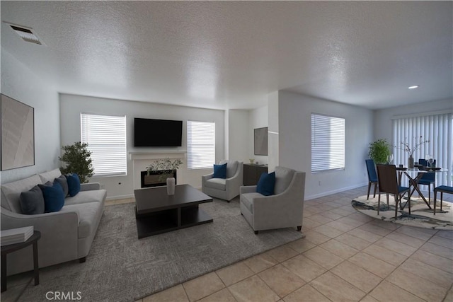 living room with a glass covered fireplace, light tile patterned flooring, baseboards, and visible vents