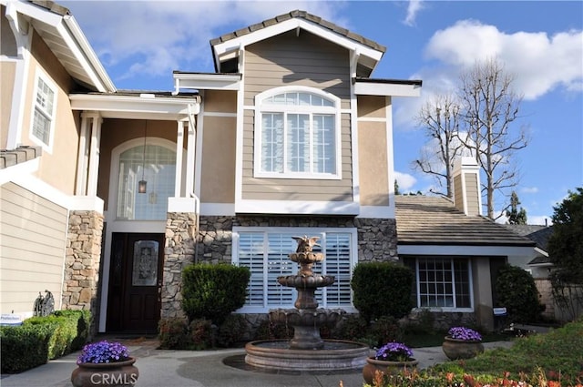 view of front facade with a chimney, stone siding, and stucco siding