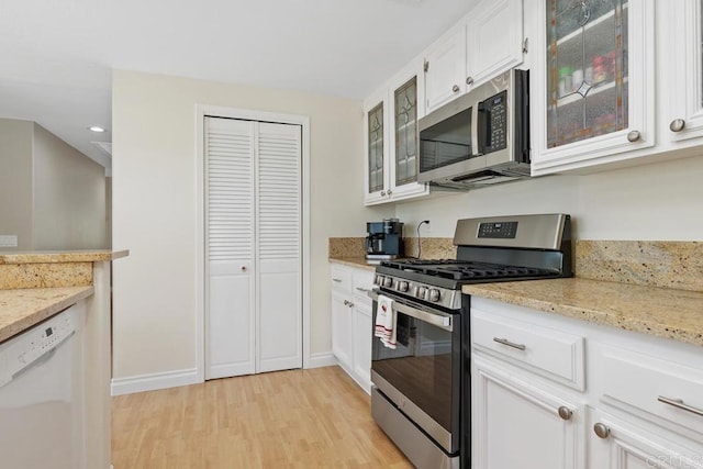 kitchen with glass insert cabinets, light stone counters, light wood-style flooring, stainless steel appliances, and white cabinetry