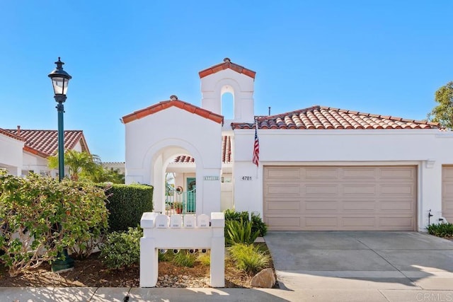 mediterranean / spanish-style home with concrete driveway, a tiled roof, an attached garage, and stucco siding