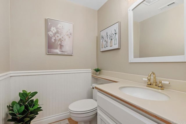 bathroom featuring vanity, toilet, visible vents, and wainscoting