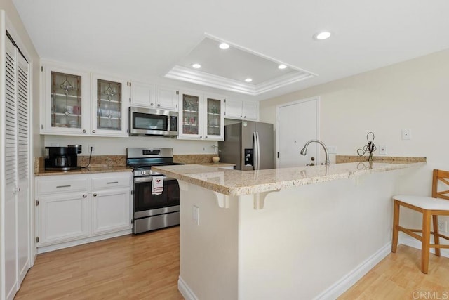 kitchen with a breakfast bar area, light wood finished floors, a peninsula, stainless steel appliances, and a raised ceiling