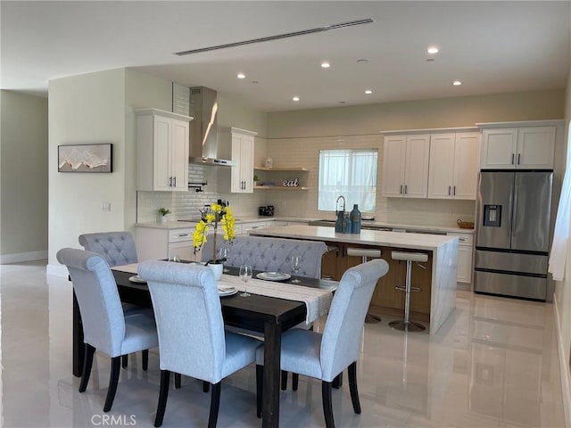 kitchen with a kitchen island, wall chimney range hood, decorative backsplash, white cabinets, and stainless steel fridge