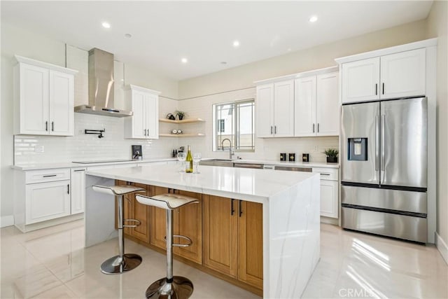 kitchen with stainless steel fridge with ice dispenser, backsplash, a kitchen island, white cabinets, and wall chimney exhaust hood