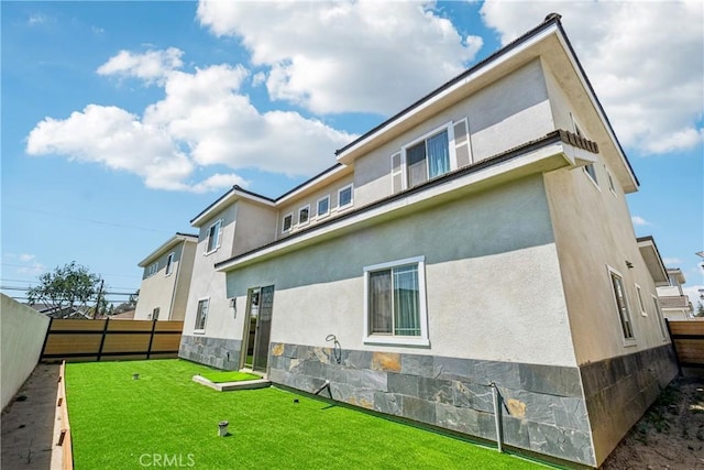 back of house featuring a yard, fence, stone siding, and stucco siding