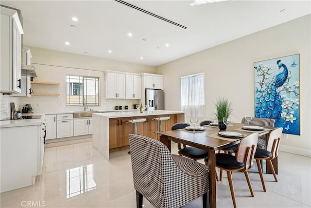 kitchen with stainless steel fridge with ice dispenser, light countertops, backsplash, a kitchen island, and a sink
