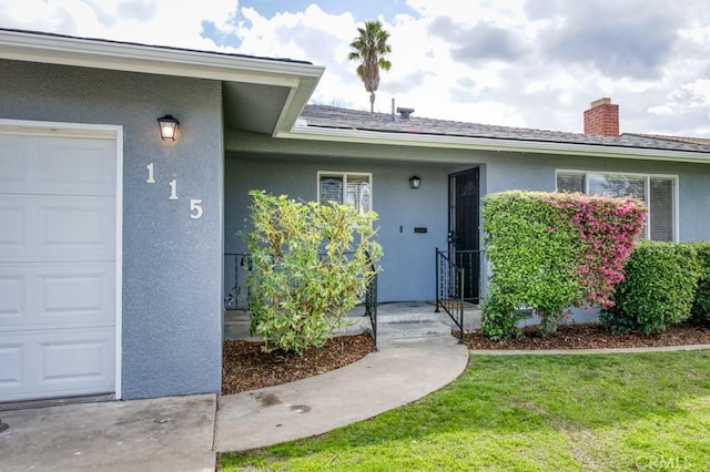 view of exterior entry featuring an attached garage, a chimney, a yard, and stucco siding