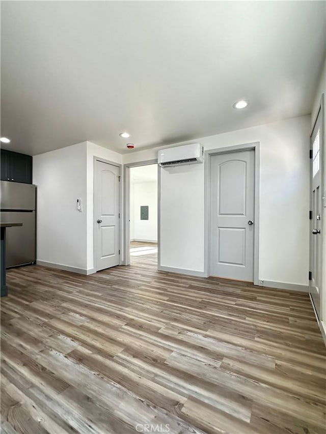 interior space featuring a wall unit AC, recessed lighting, baseboards, and light wood finished floors