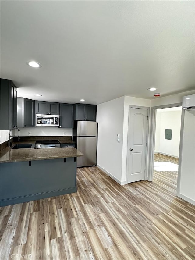 kitchen with dark stone countertops, a peninsula, light wood-style flooring, a sink, and stainless steel appliances