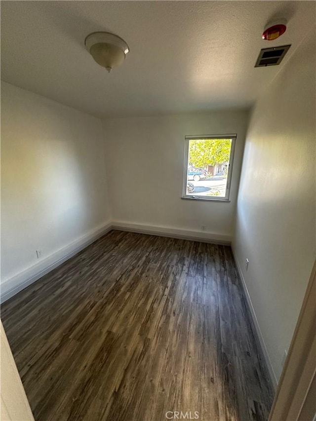 empty room featuring visible vents, a textured ceiling, dark wood-type flooring, and baseboards