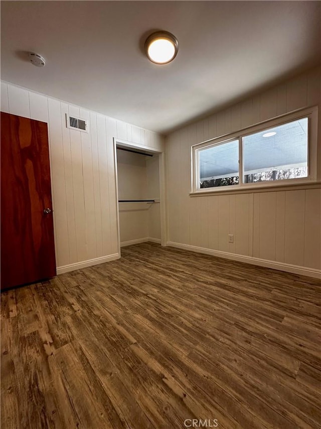 unfurnished bedroom with a closet, baseboards, visible vents, and dark wood-style flooring