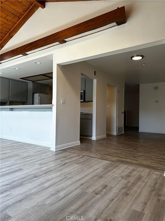 empty room featuring lofted ceiling with beams, baseboards, and wood finished floors