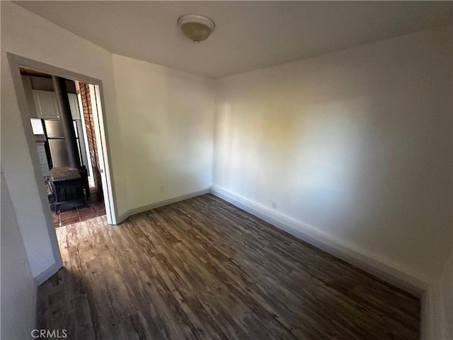 unfurnished room with a wood stove, dark wood-style floors, and baseboards