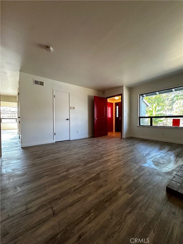 unfurnished living room with dark wood-style floors, visible vents, and baseboards