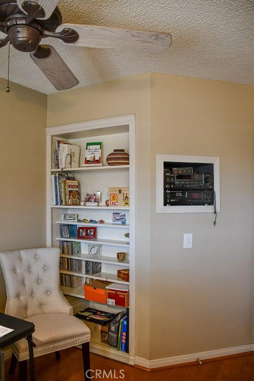 living area featuring baseboards, a textured ceiling, and ceiling fan