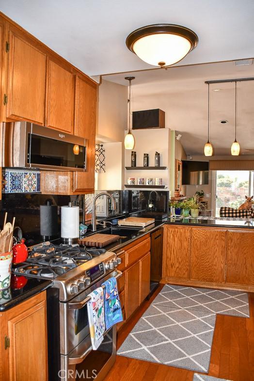 kitchen with dark countertops, wood finished floors, brown cabinetry, stainless steel appliances, and a sink