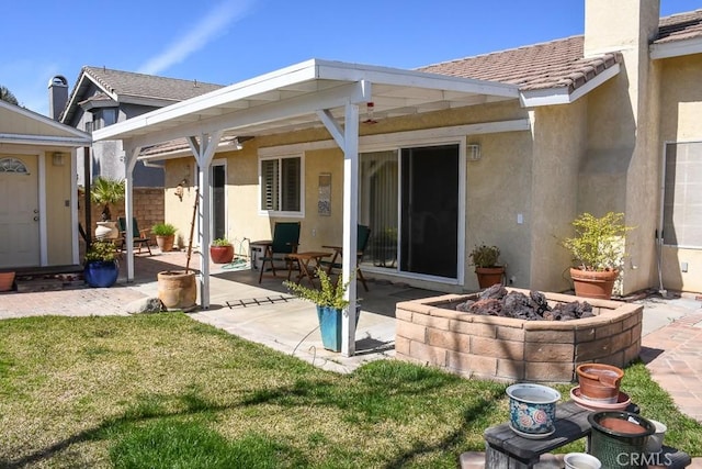 back of house with stucco siding, a lawn, a tile roof, a patio, and a fire pit