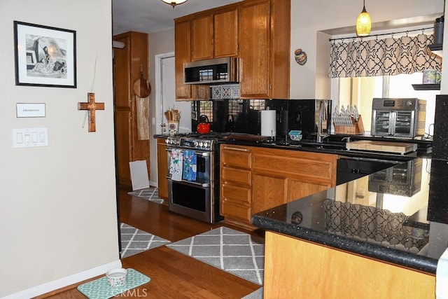 kitchen featuring brown cabinets, dark stone countertops, stainless steel appliances, decorative backsplash, and dark wood-style flooring