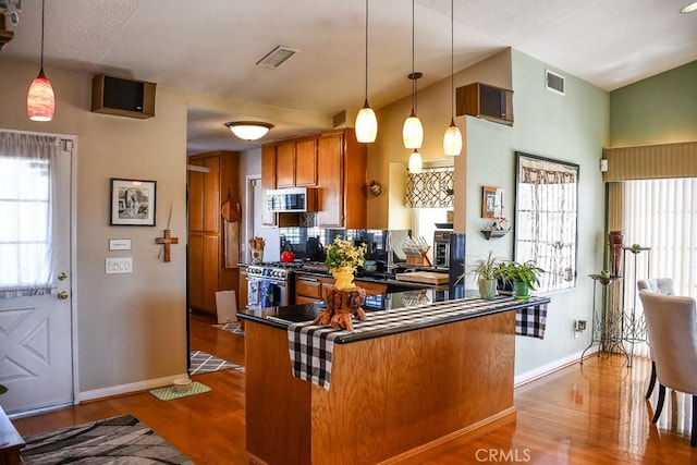 kitchen featuring visible vents, dark countertops, appliances with stainless steel finishes, and brown cabinetry