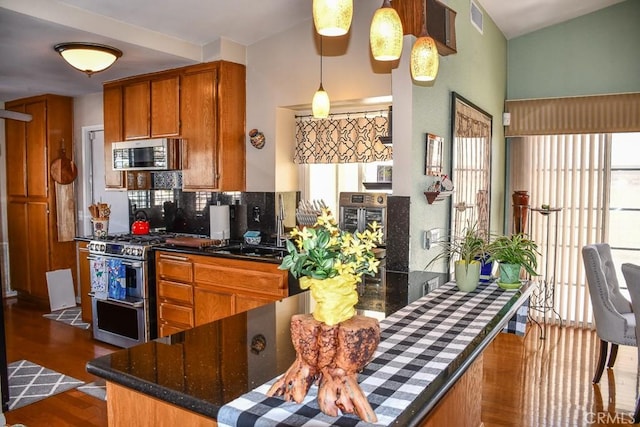 kitchen with visible vents, dark wood-type flooring, pendant lighting, brown cabinets, and appliances with stainless steel finishes