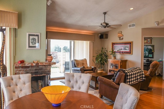 dining room with visible vents, a ceiling fan, wood finished floors, lofted ceiling, and a brick fireplace