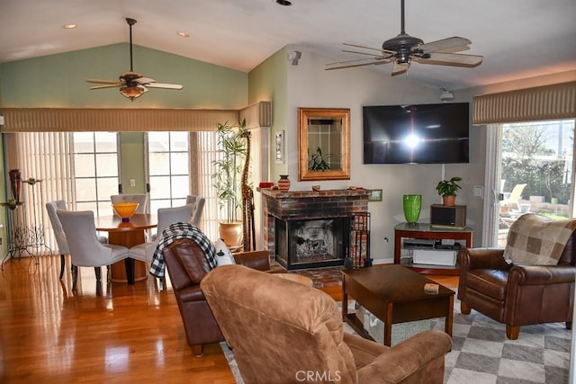 living area with a ceiling fan, wood finished floors, a fireplace, and vaulted ceiling