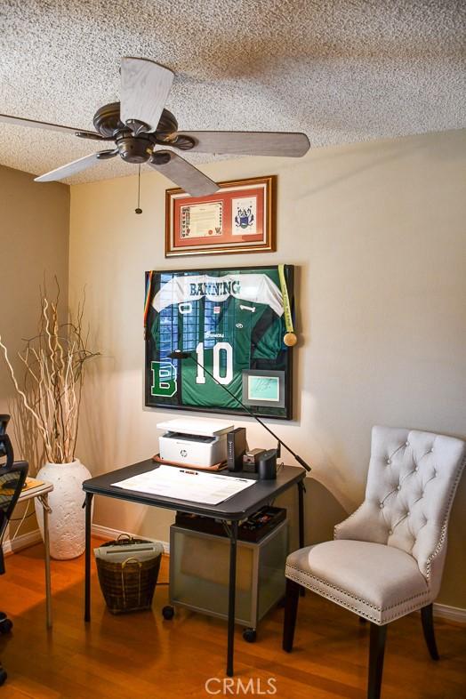 living area featuring ceiling fan, wood finished floors, baseboards, and a textured ceiling