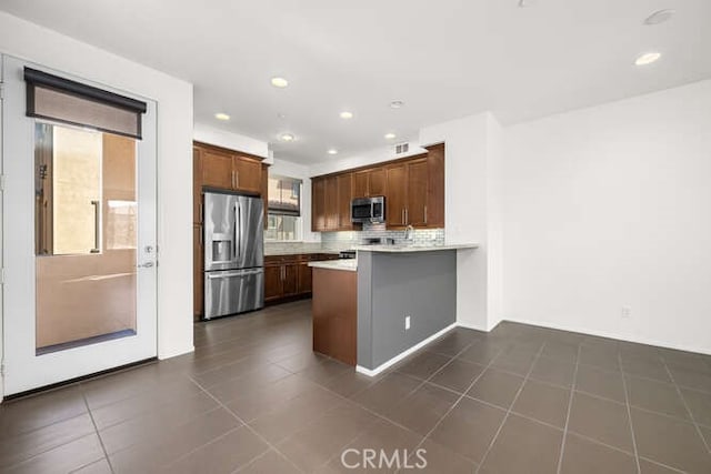 kitchen with backsplash, dark tile patterned floors, light countertops, appliances with stainless steel finishes, and a peninsula