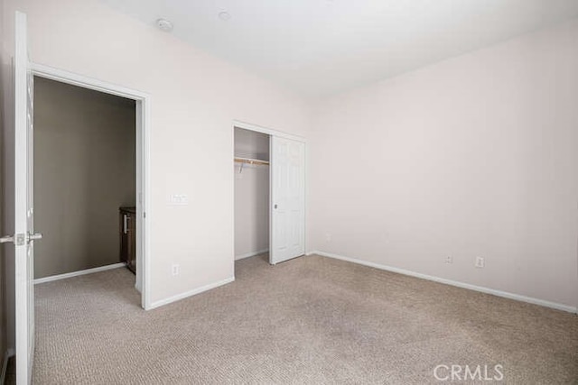 unfurnished bedroom with a closet, baseboards, and light colored carpet