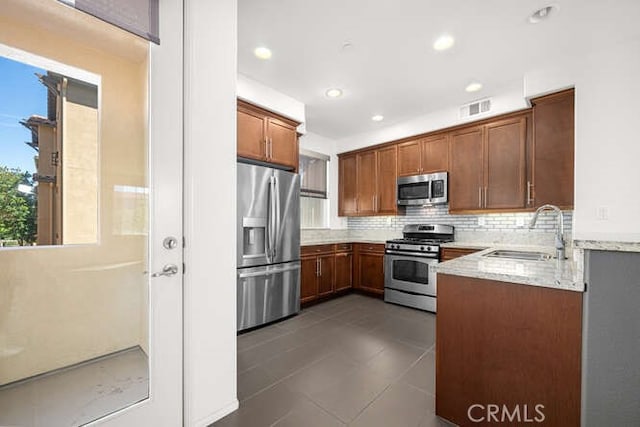 kitchen with light stone countertops, visible vents, a sink, stainless steel appliances, and backsplash