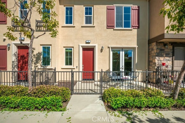 doorway to property with stucco siding, french doors, and fence