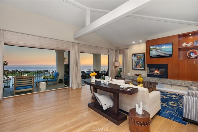 living room featuring a glass covered fireplace, lofted ceiling with beams, a water view, and wood finished floors