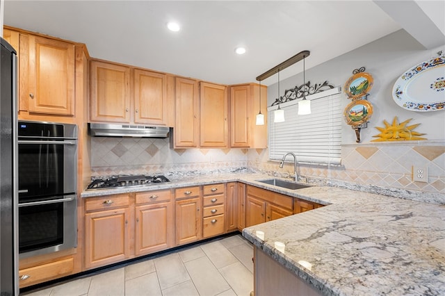 kitchen featuring light stone countertops, a sink, hanging light fixtures, under cabinet range hood, and appliances with stainless steel finishes