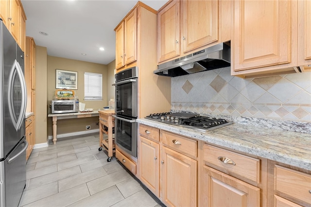 kitchen featuring light stone countertops, light brown cabinetry, decorative backsplash, stainless steel appliances, and under cabinet range hood