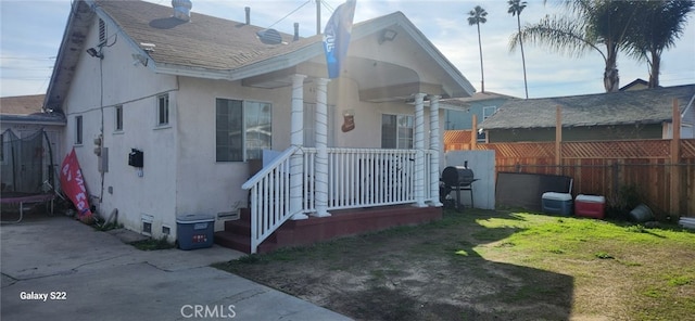 view of property exterior with stucco siding, a lawn, a shingled roof, and fence