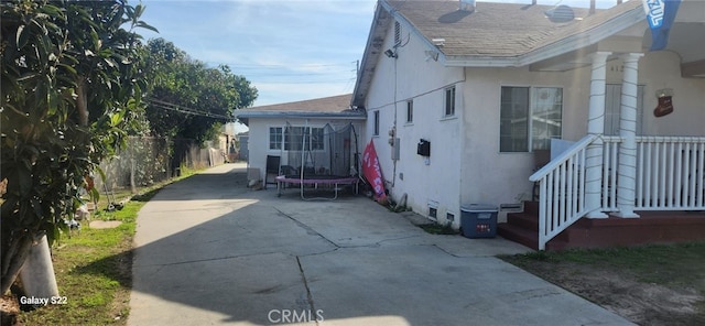 view of property exterior featuring a patio area, stucco siding, a trampoline, and fence