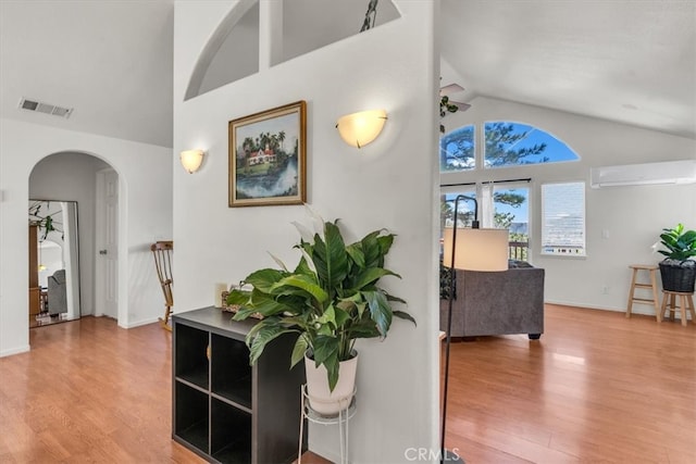 foyer featuring visible vents, a wall mounted air conditioner, wood finished floors, arched walkways, and high vaulted ceiling