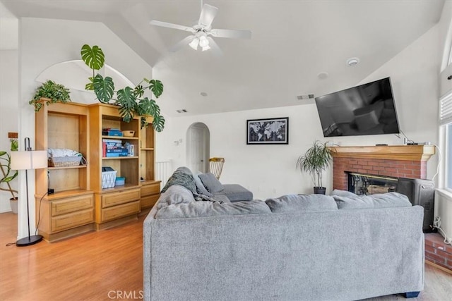 living room featuring a ceiling fan, light wood-style flooring, a fireplace, arched walkways, and vaulted ceiling